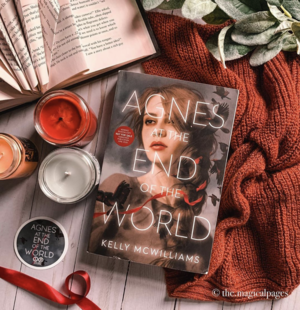 Picture of 'Agnes at the End of the World' on a table with candles and a sweater