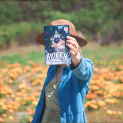 Katrina Leno holding up the book 'Horrid' by Katrina Leno, in a field during the day